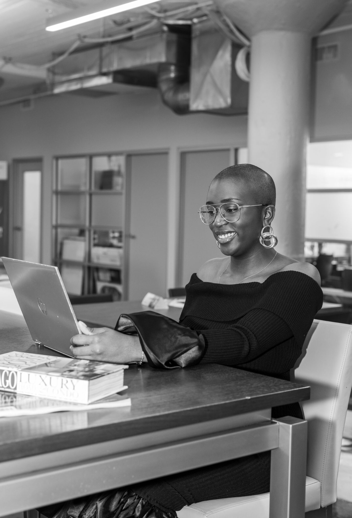 Junia Janvier smiling at a laptop in a bright office, black-and-white photo.