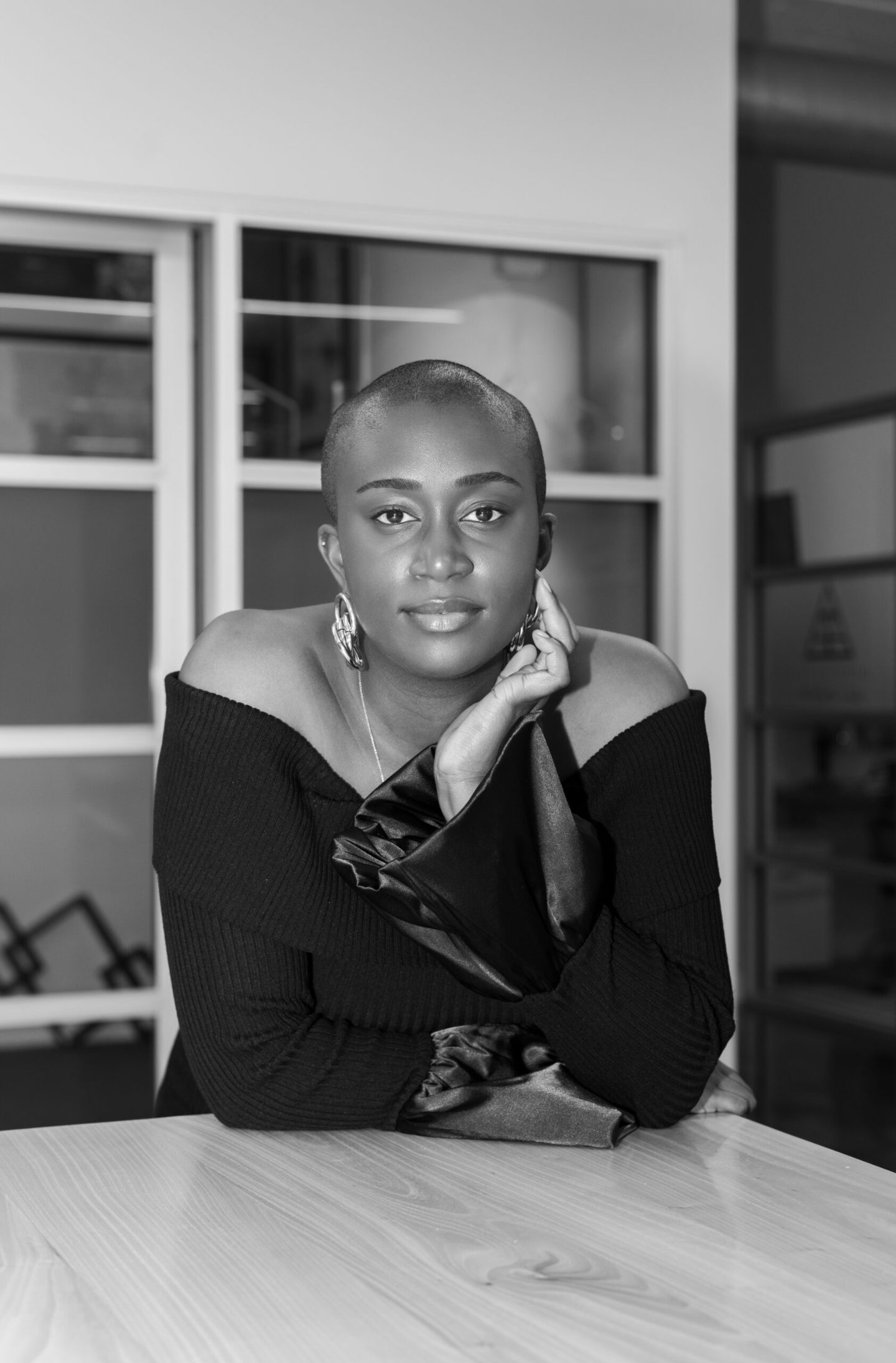 Black-and-white portrait of Junia Janvier seated at a table, chin resting on her hand
